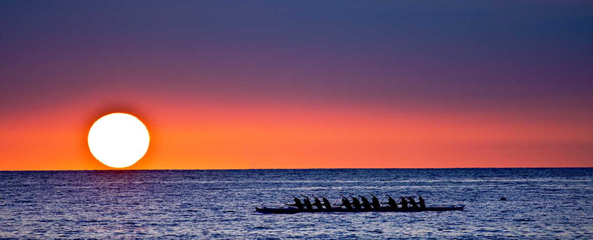 group of people rowing a canoe during sunset